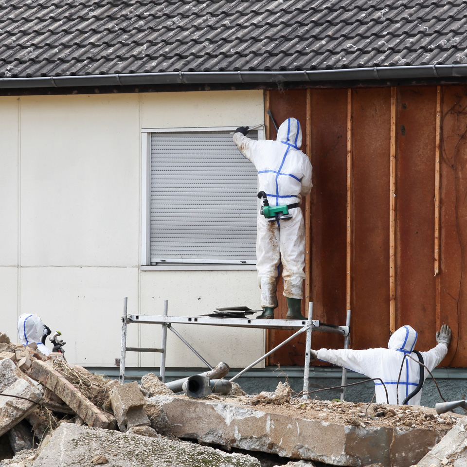 Fachleute in Schutzanzügen entfernen Asbest an einer Wand